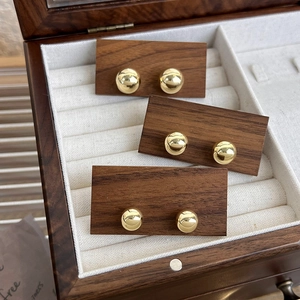 Vue détaillée des boucles d'oreilles boules dorées polies sur un présentoir en bois vintage