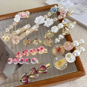 Detailed close-up of handmade retro hair clips with dried flowers and pearls on glass tray