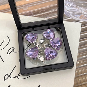Detailed macro view of five purple rhinestone heart hair clips in a black display box