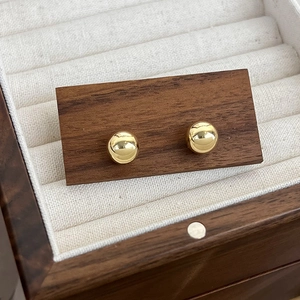 Détail de boucles d'oreilles boules dorées polies sur un plateau à bijoux en bois