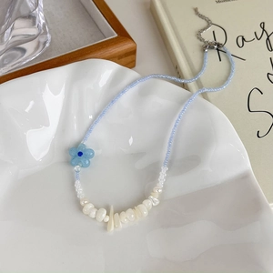 Détail d'un collier de perles bleu avec fleur et perles blanches sur un plat en céramique
