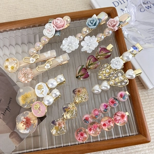 Detailed macro view of vintage hair clips with resin roses, pearls, and dried flowers