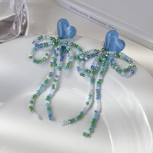 Détail des boucles d'oreilles cœur bleu avec nœud en perles et longues franges