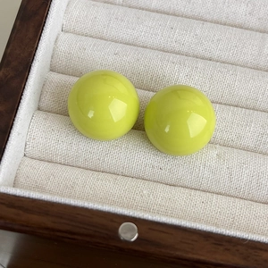 Dettaglio di orecchini a lobo in resina verde lime su un espositore in velluto beige