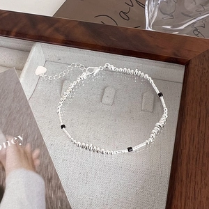 Close-up of beaded silver bracelet with black square accents and heart charm on wooden tray