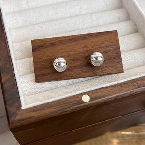 Gros plan de boucles d'oreilles boules argentées sur support noyer dans un écrin en bois
