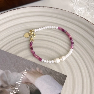 Détail d'un bracelet en perles d'eau douce avec perles mauves et pendentif cœur doré sur plateau