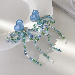 Détail de boucles d'oreilles pompons à perles avec cœur bleu et nœud suspendues sur une assiette