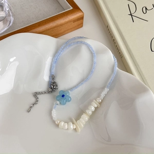 Détail du collier de perles bleues avec pendentif fleur sur une assiette blanche