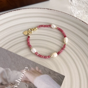 Détail d'un bracelet en perles roses et blanches avec un pendentif cœur doré