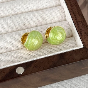 Close-up of golden huggie earrings with green marble enamel in a velvet jewelry box