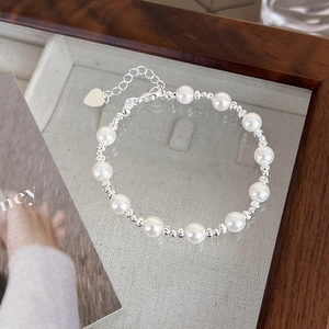 Detail view of retro silver beaded bracelet with pearls and a heart charm on glass surface