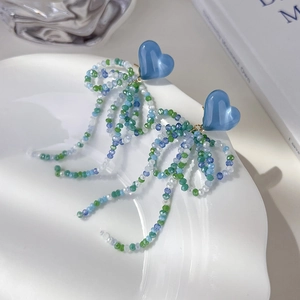 Gros plan de boucles d'oreilles cœur bleu avec longs pompons de perles sur porcelaine