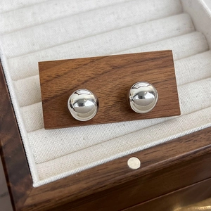 Gros plan de boucles d'oreilles boules en argent poli sur un support à bijoux en noyer