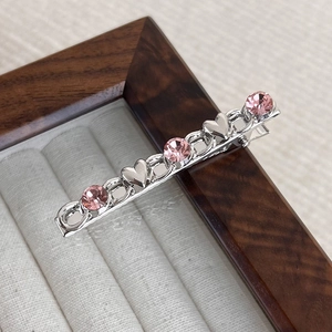 Macro view of silver alloy hair clip with pink crystals and heart shapes on wood