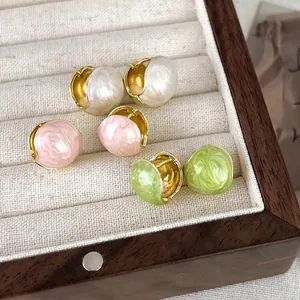 Three pairs of French bean-shaped hoop earrings in pink, white, and green on beige velvet