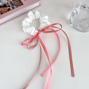 Gros plan d'un chouchou en satin blanc avec un long ruban rose sur un bureau blanc