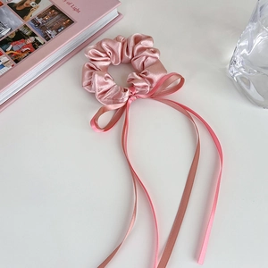 Vue détaillée du chouchou en satin de soie rose avec ruban et nœud sur bureau blanc