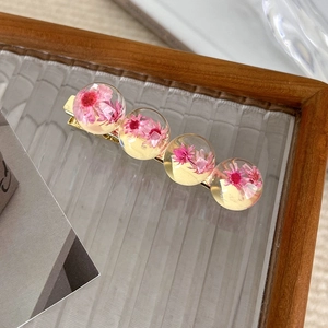 Close-up of golden hair clip with four clear resin spheres containing real pink dried flowers