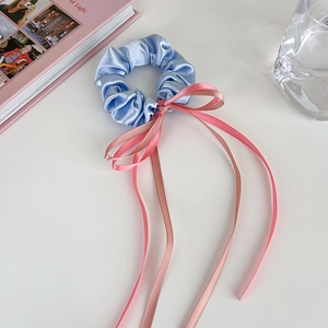 Gros plan sur chouchou en satin bleu avec longs rubans roses sur bureau blanc