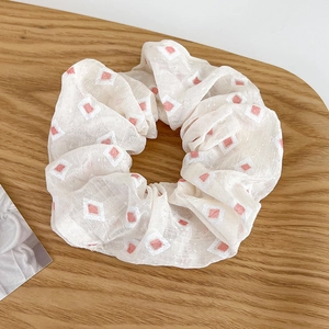 Detalle de coletero de encaje crema con patrón de diamantes rosa sobre fondo de madera clara