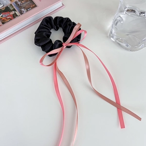 Chouchou en satin noir avec un long ruban rose disposé à plat sur une surface blanche