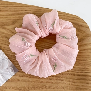 Detalle de coletero de gasa rosa con bordado floral sobre una bandeja de madera