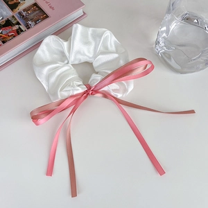 Détail d'un chouchou en satin blanc avec un long ruban rose sur un bureau blanc