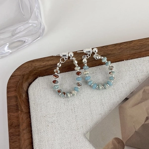 Detail of beaded hoop earrings with blue and brown stones on white linen fabric