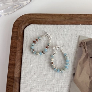 Detail view of retro beaded hoop earrings with blue and brown stones on linen