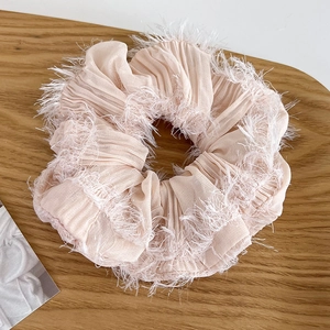 Detalle de coletero plisado rosa claro con bordes de flecos sobre madera suave