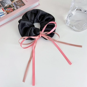 Détail d'un chouchou en satin noir avec rubans roses posé sur un bureau blanc épuré