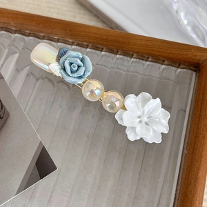 Detail of vintage blue rose hair clip with pearls and white petals on gold metal base