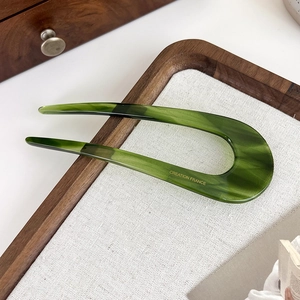 Détail d'un pic à cheveux en U en acétate vert foncé avec motif marbré sur plateau
