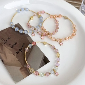 Detail of four colorful beaded bracelets with gold chains and star charms on white ceramic
