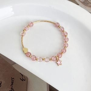 Detail of pink strawberry quartz beads with gold heart and star charms on a white plate