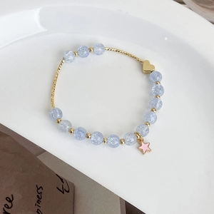 Detail of light blue beaded bracelet with gold heart and pink star charms on white ceramic