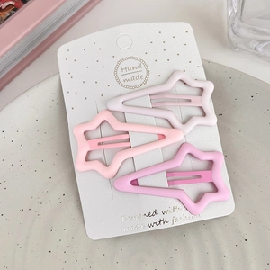 Detailed close-up of three matte star-shaped hair clips in pink and white tones