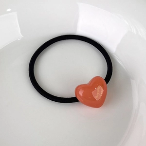Detail of pink heart-shaped acrylic hair tie with gold lettering on white ceramic tray