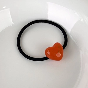 Detail of candy-colored heart pendant on a black elastic hair tie on a white plate