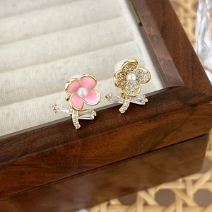 Detail of asymmetric zircon flower earrings with pink enamel and pearls on wood box
