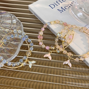 Detailed view of beaded bracelets with gradient mermaid tail pendants in glass tray