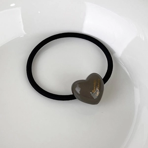 Close-up of minimalist heart hair tie with golden lettering on a white porcelain plate