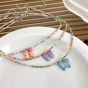 Colliers en perles colorées avec pendentifs papillon pailletés sur assiette blanche