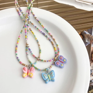 Détail de trois colliers de perles colorées avec pendentifs papillon en résine aux tons pastels