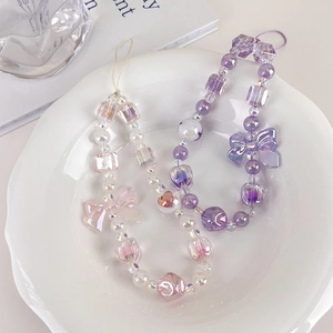 Detailed macro view of purple and pink bead phone charms with large translucent bows in a dish