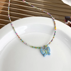 Détail du collier de perles colorées avec pendentif papillon bleu sur un plateau céramique
