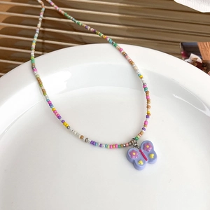 Gros plan d'un collier de perles colorées avec un pendentif papillon lilas sur une assiette