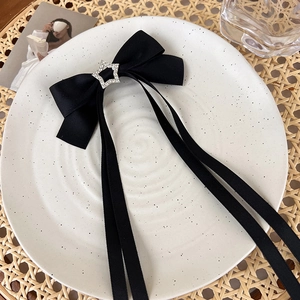 Detail of black satin bow hair clip with silver star rhinestone center and long ribbon