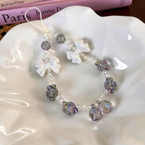 Macro view of purple floral beaded phone charm with white bows on a textured plate